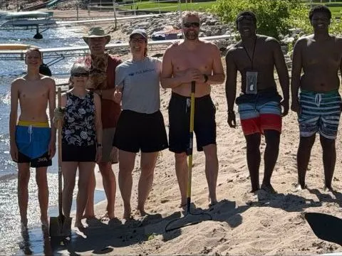 Volunteers standing on a lakeshore beach with a rake and a shovel.