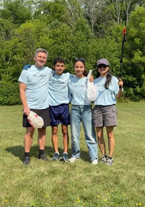 Four volunteers in light blue Global Day of Service T-shirts holding litter bags and a litter picker in a green field.